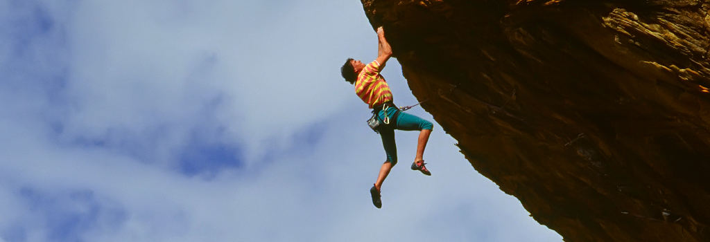 Rock climber struggles for his next grip on a challenging ascent.